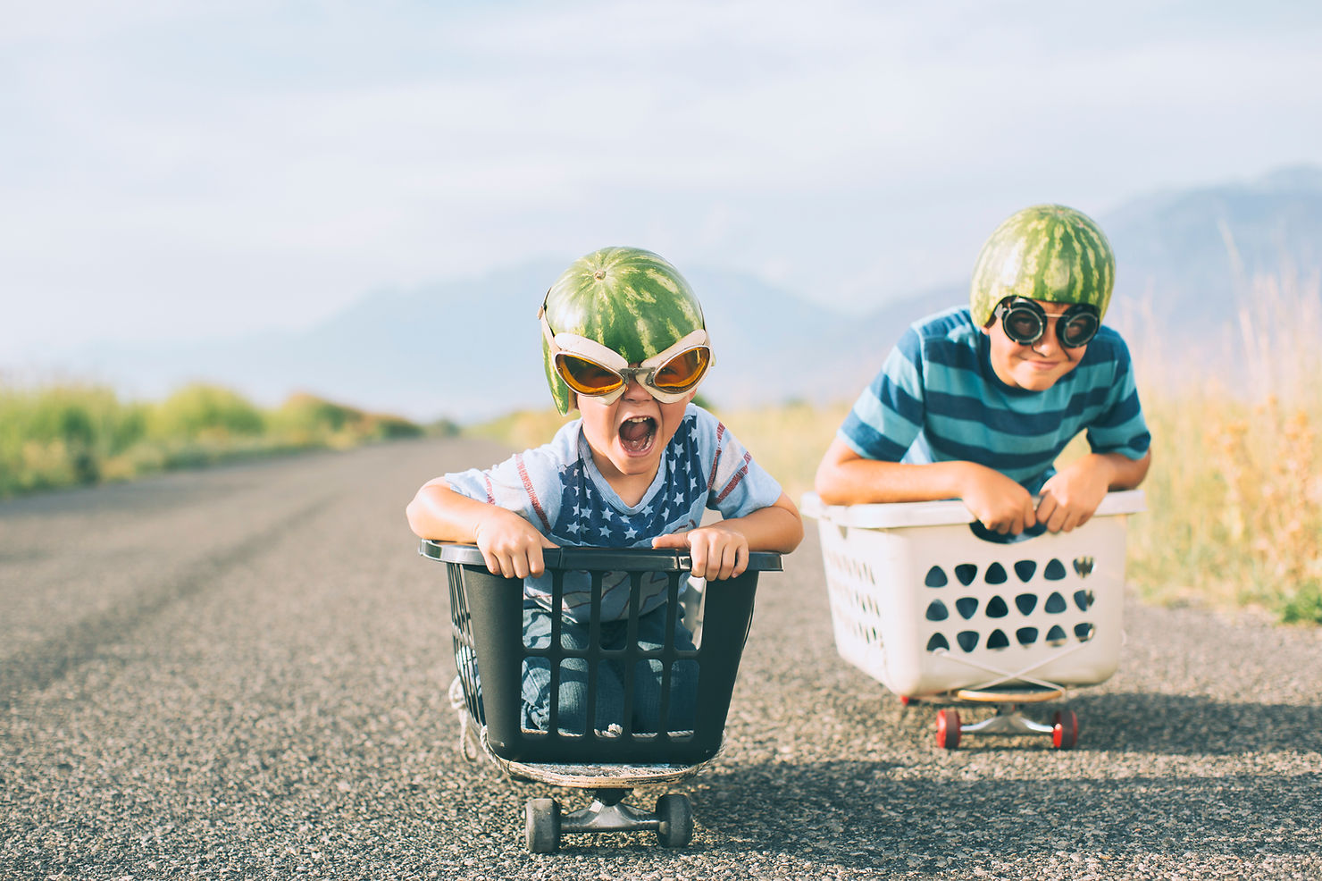 Two children racing in laundry baskets balanced on skateboards